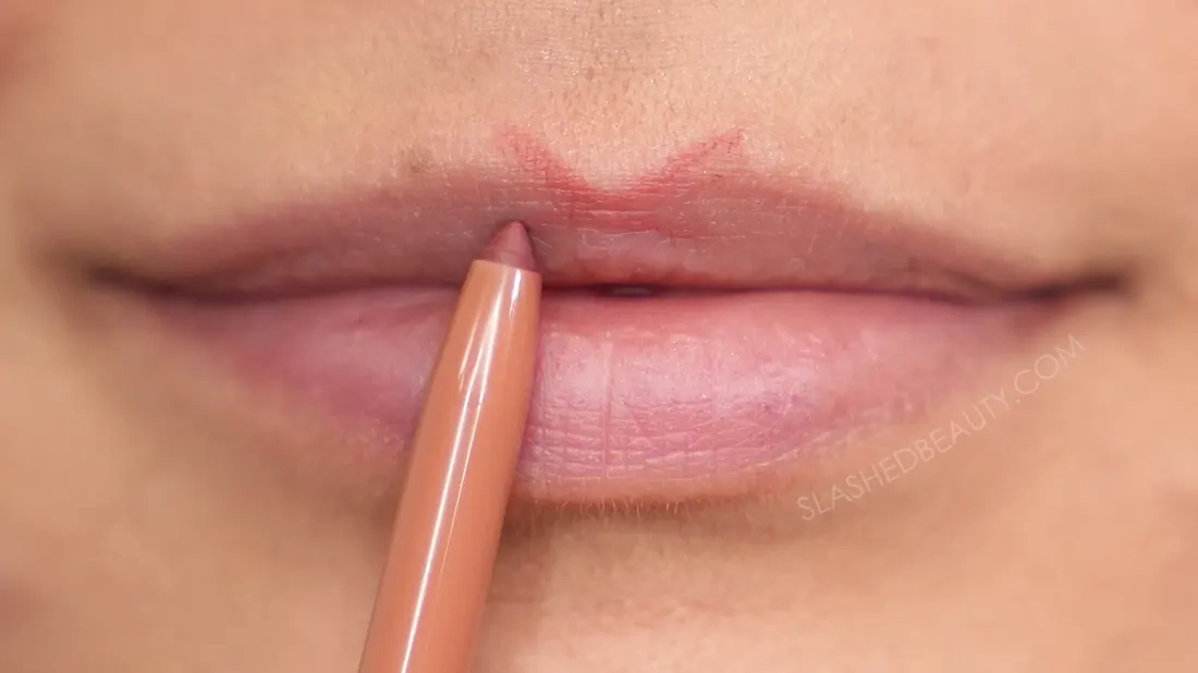 Close up of lip liner on lips drawn in an X shape on the cupid's bow. | How to Make Your Lips Look Bigger with Makeup | Slashed Beauty