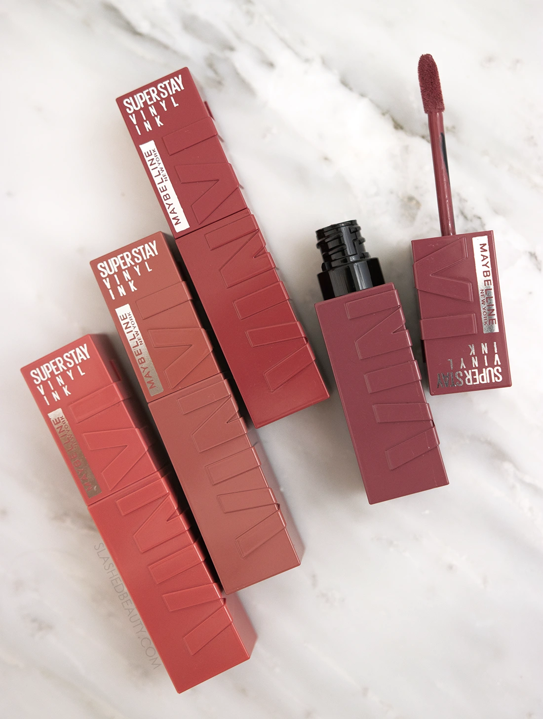 Tubes of Maybelline Superstay Vinyl Ink Liquid Lipstick lying flat on a marble surface | Maybelline Superstay Vinyl Ink Liquid Lipsticks Review | Slashed Beauty