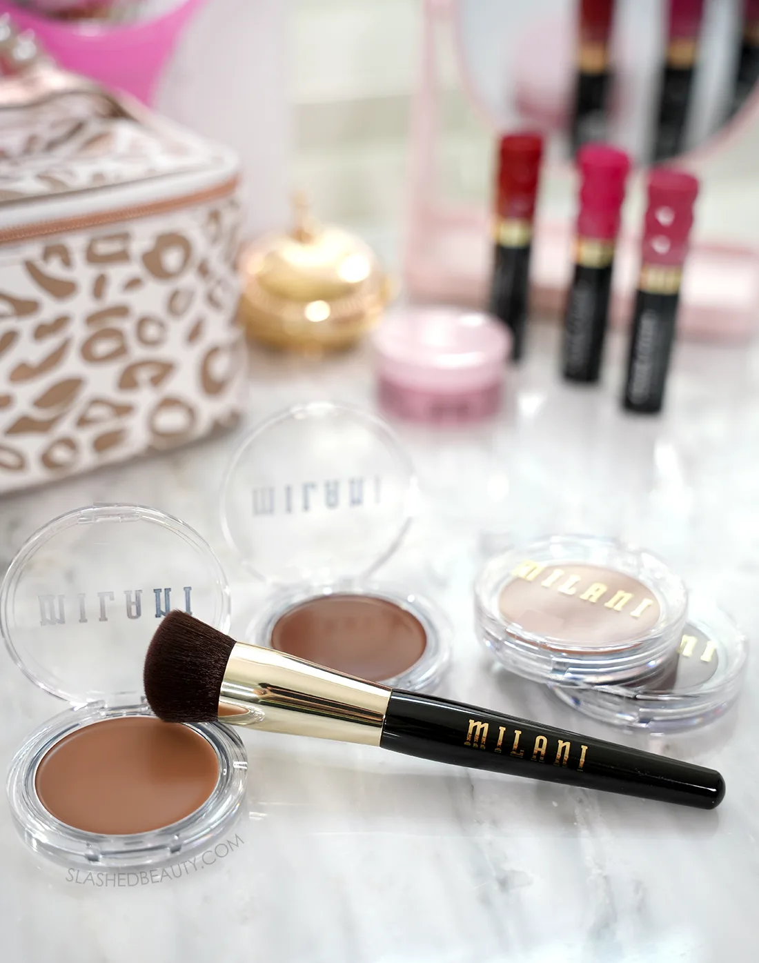 Milani Cheek Kiss Cream Bronzers stacked and open on a marble vanity with the Milani Face Buffing Brush F220. | Milani Cheek Kiss Cream Bronzers Review | Slashed Beauty