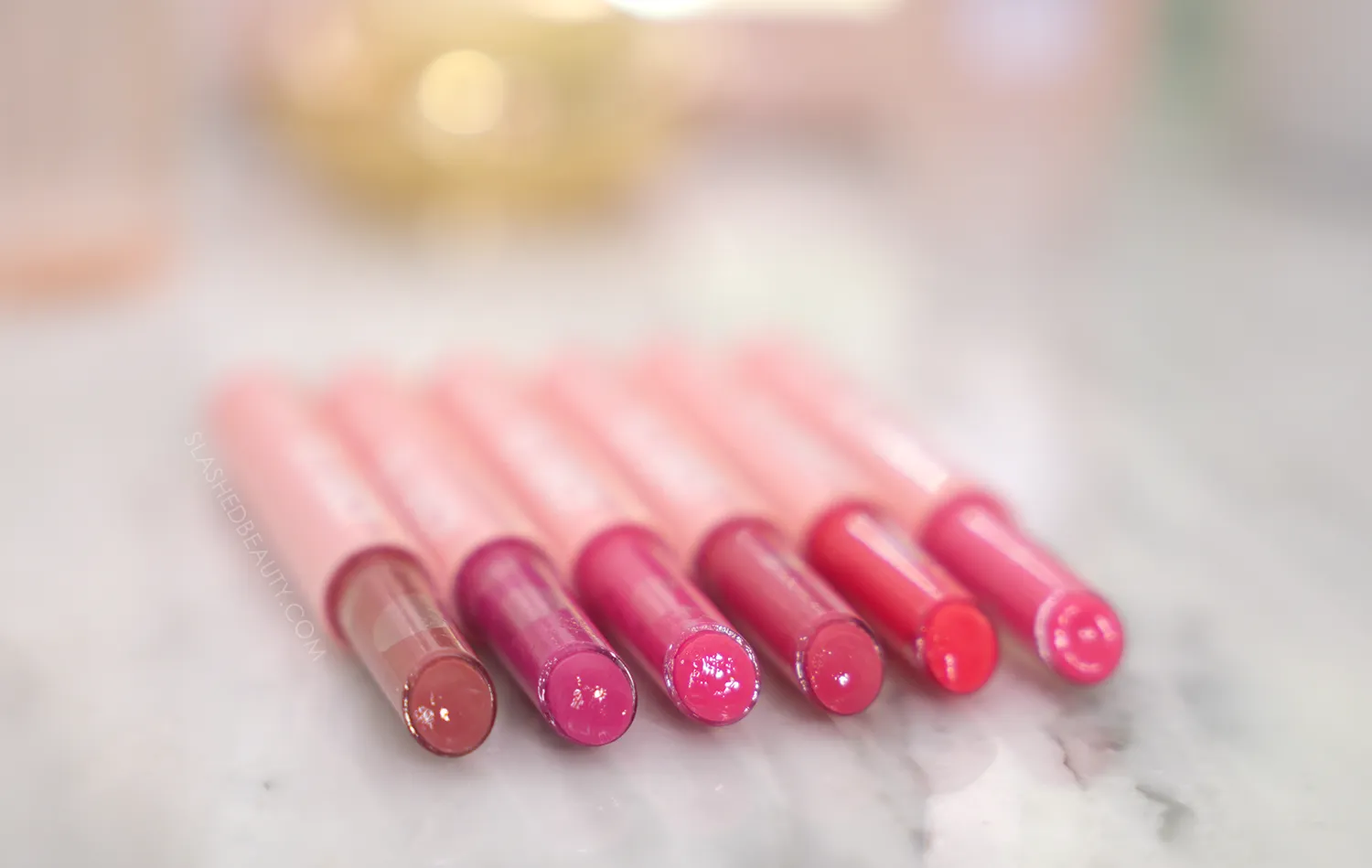 Six tubes of ColourPop So Juicy Gloss Balms lying side by side with the caps off, revealing glossy color | ColourPop So Juicy Plumping Gloss Balms Review | Slashed Beauty